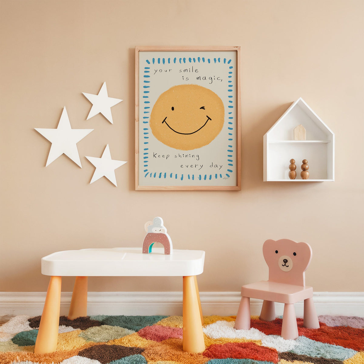 Winking smiley face quote nursery print in an oak frame on a peach wall above a kids table with wall stars