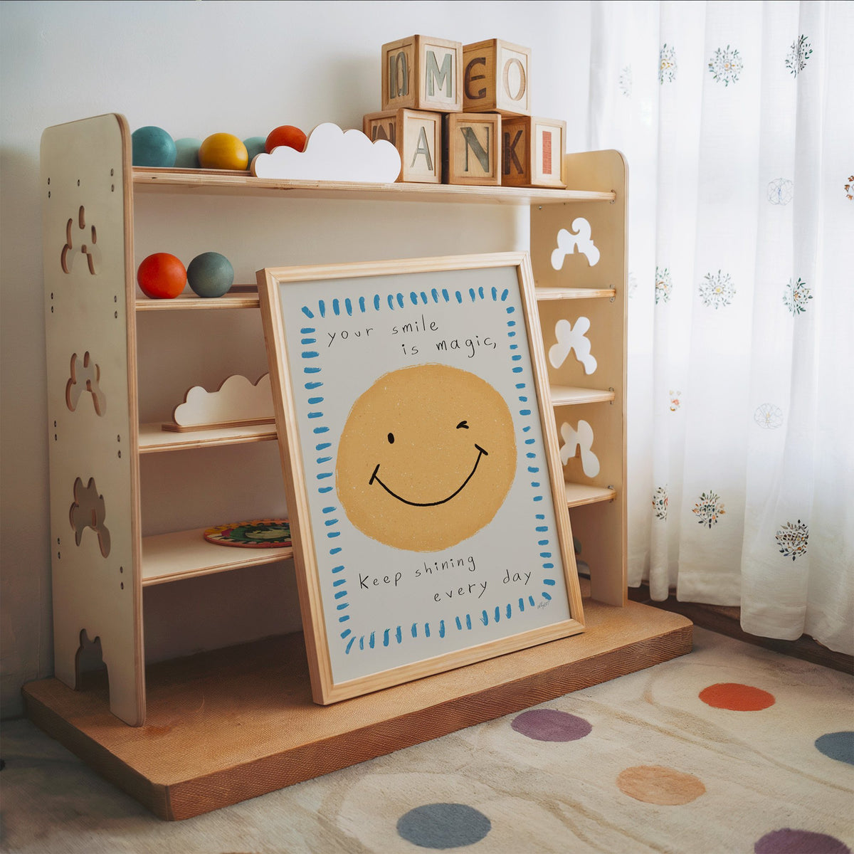 Winking smiley face quote nursery print in an oak frame leaning on a toy shelf with wooden letter blocks