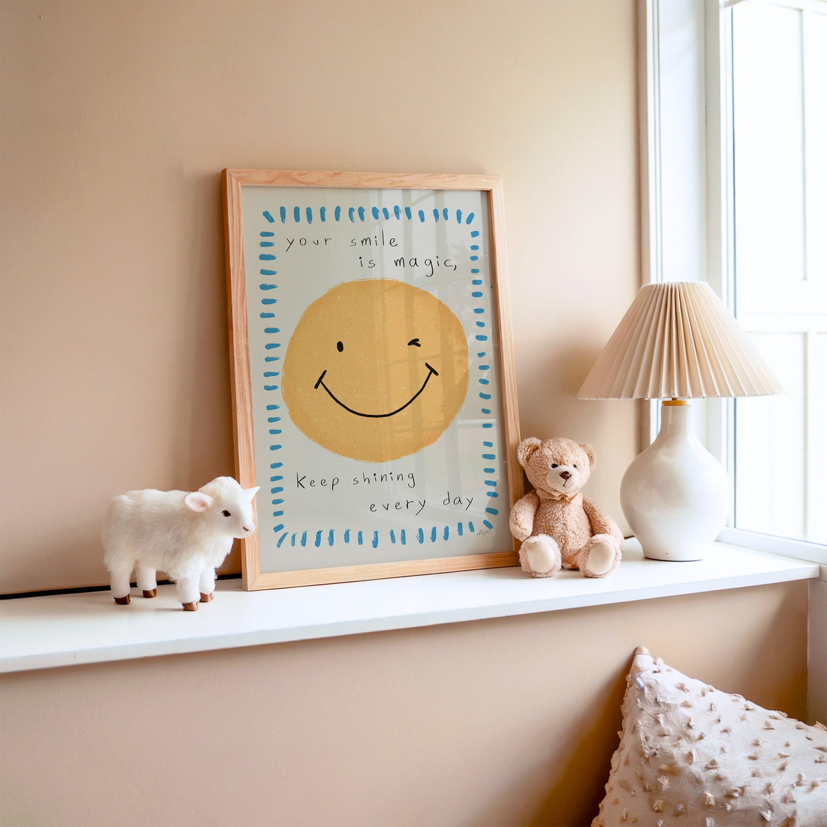 Winking smiley face quote nursery print in an oak frame on a window ledge with a toy lamb and teddy