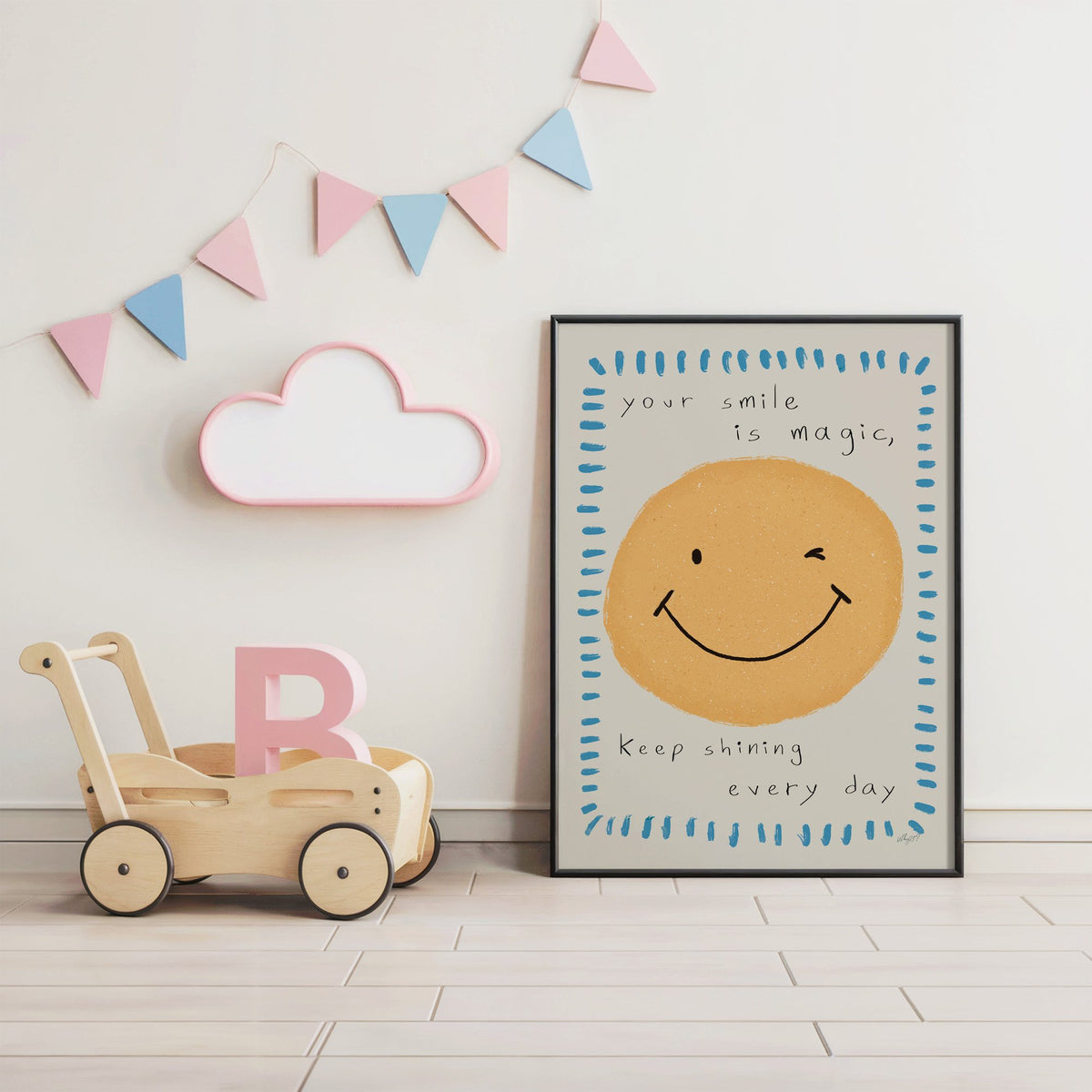 Winking smiley face quote nursery print in a black frame under pastel bunting by a wooden baby walker