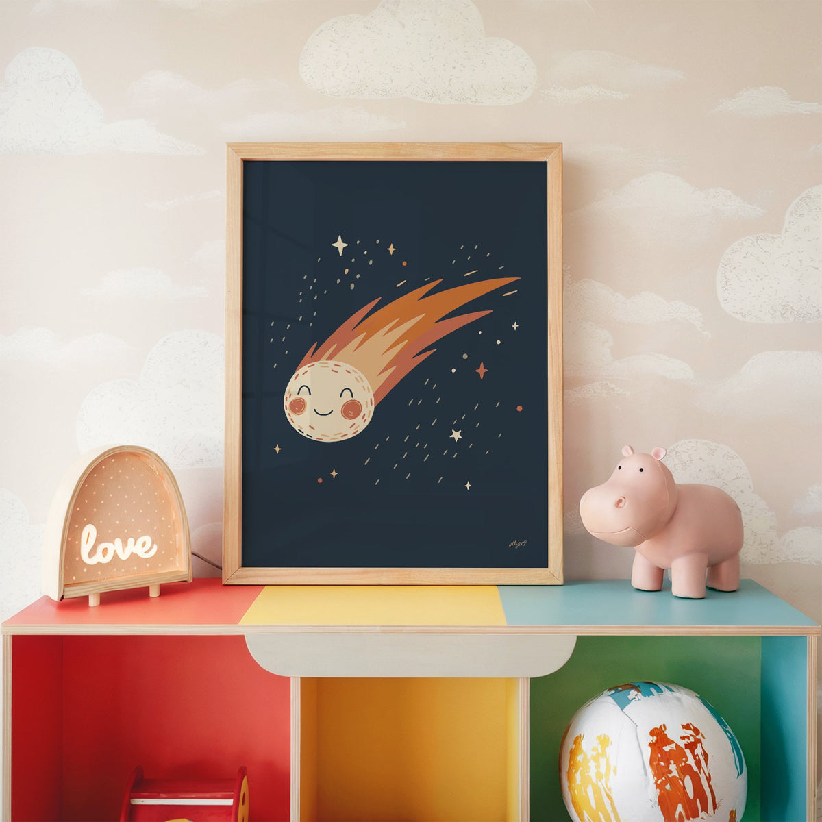 Smiling comet with fiery tail nursery print in an oak frame on a rainbow toy shelf against cloud wallpaper