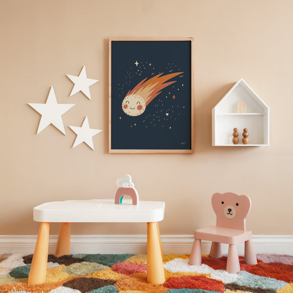Smiling comet with fiery tail nursery print in an oak frame on a peach wall above a kids table with wall stars