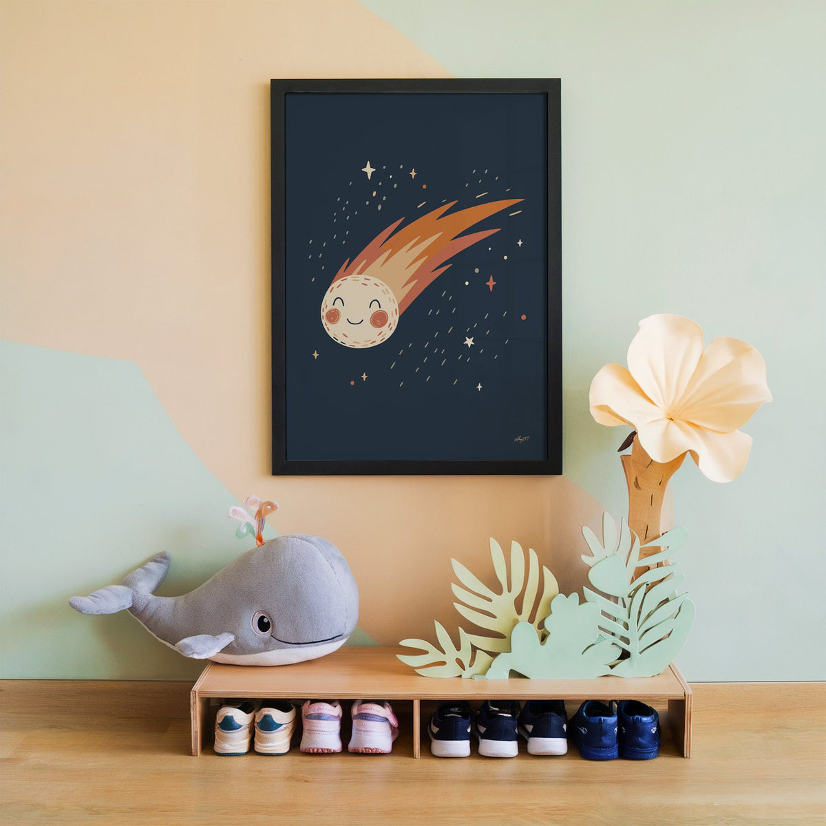 Smiling comet with fiery tail nursery print in a black frame on a mint and peach wall above a whale plush