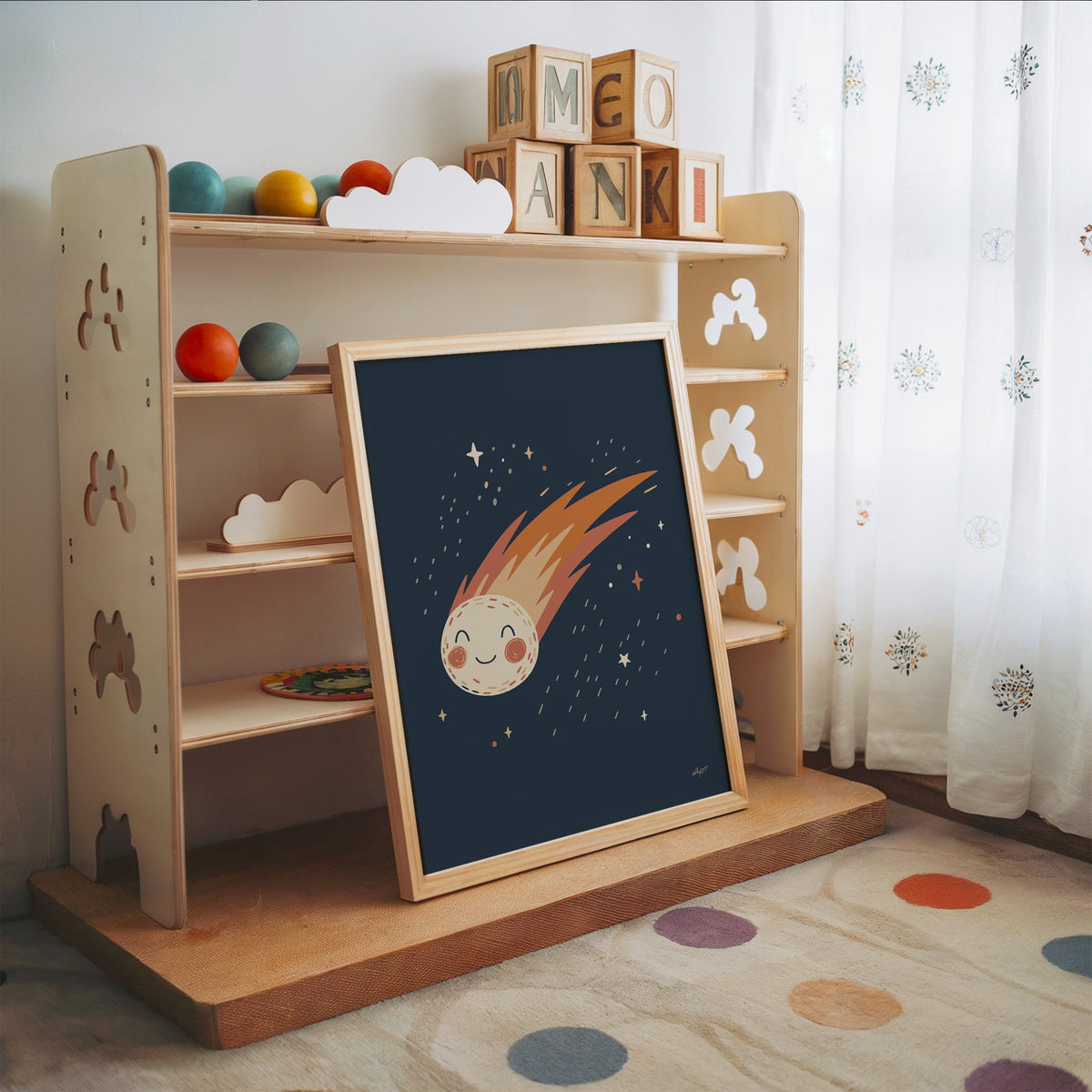 Smiling comet with fiery tail nursery print in an oak frame leaning on a toy shelf with wooden letter blocks