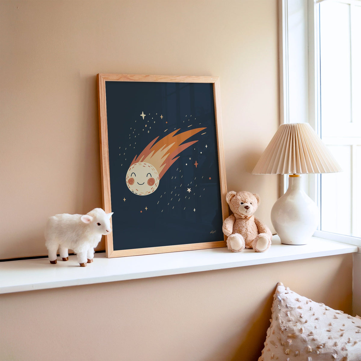 Smiling comet with fiery tail nursery print in an oak frame on a window ledge with a toy lamb and teddy