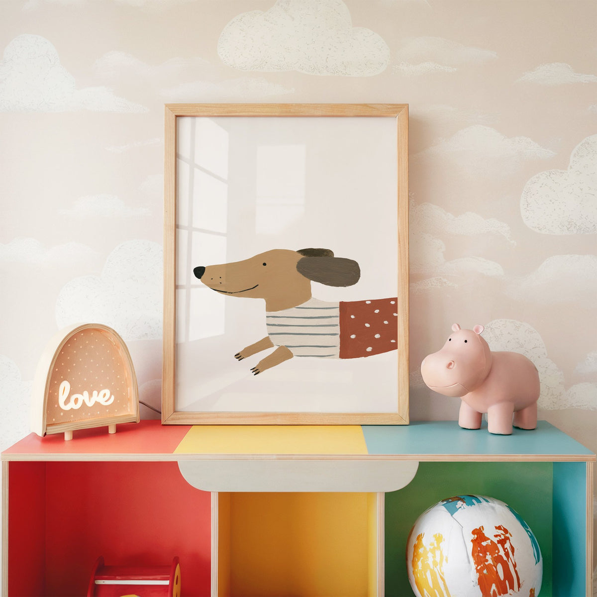 Smiling dachshund close-up nursery print in an oak frame on a rainbow toy shelf against cloud wallpaper