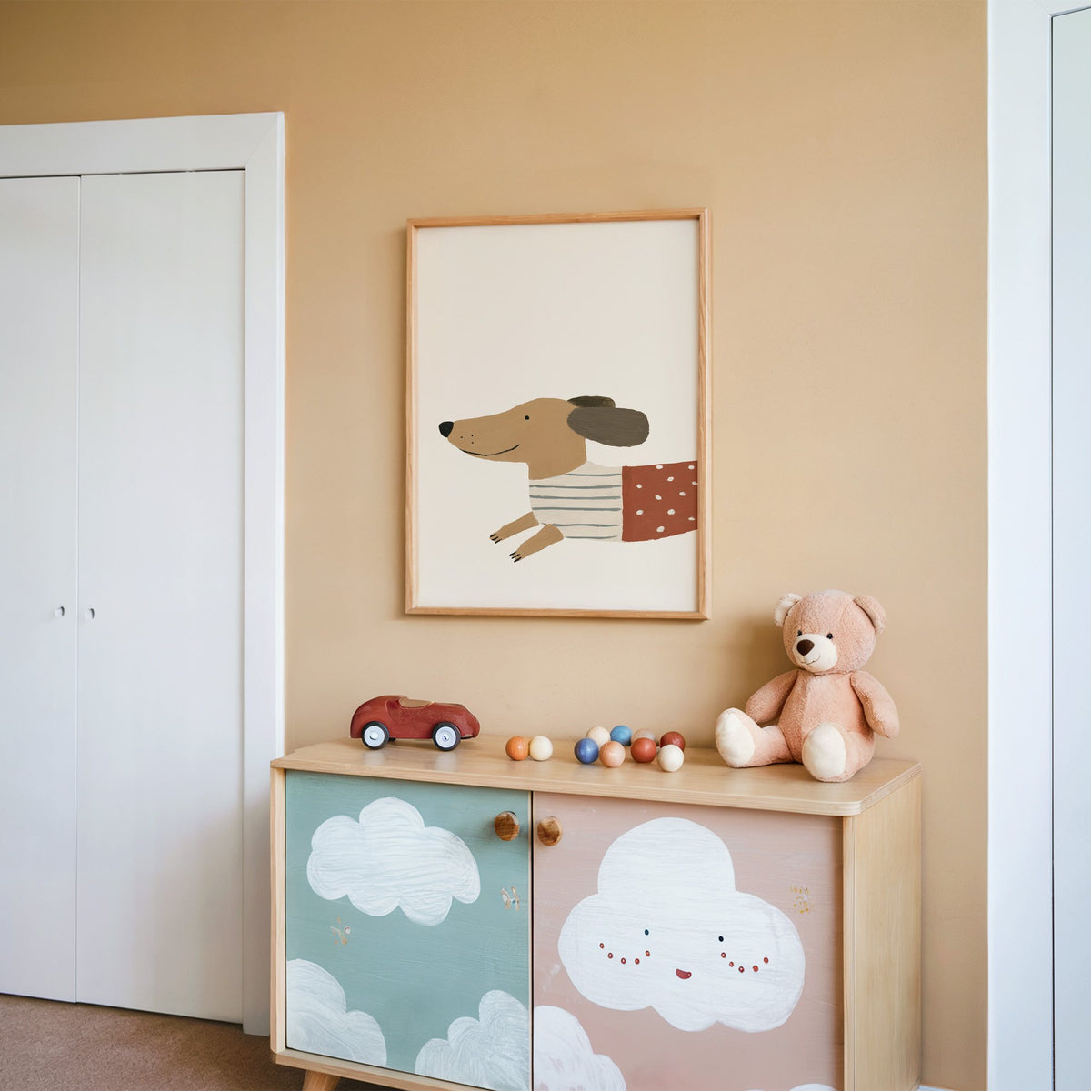 Smiling dachshund close-up nursery print in an oak frame on a peach wall above a cloud-painted cabinet