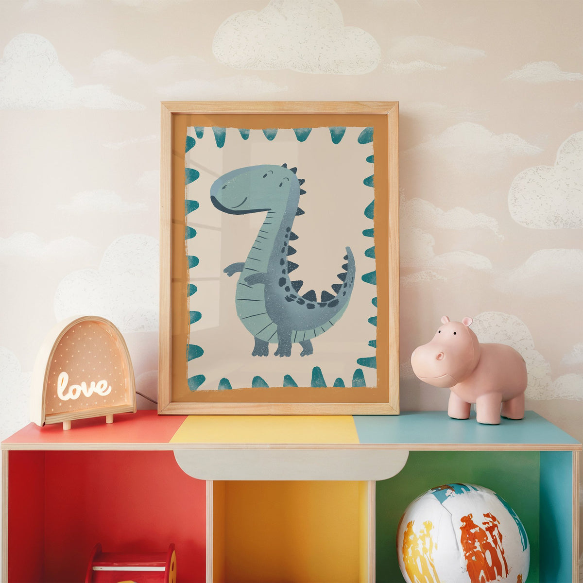 Smiling teal dinosaur nursery print in an oak frame on a rainbow toy shelf against cloud wallpaper