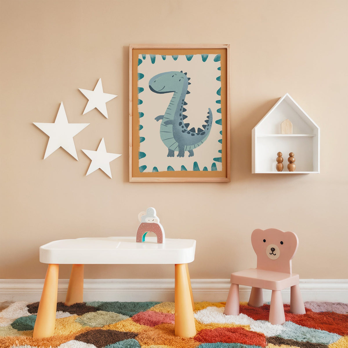Smiling teal dinosaur nursery print in an oak frame on a peach wall above a kids table with wall stars
