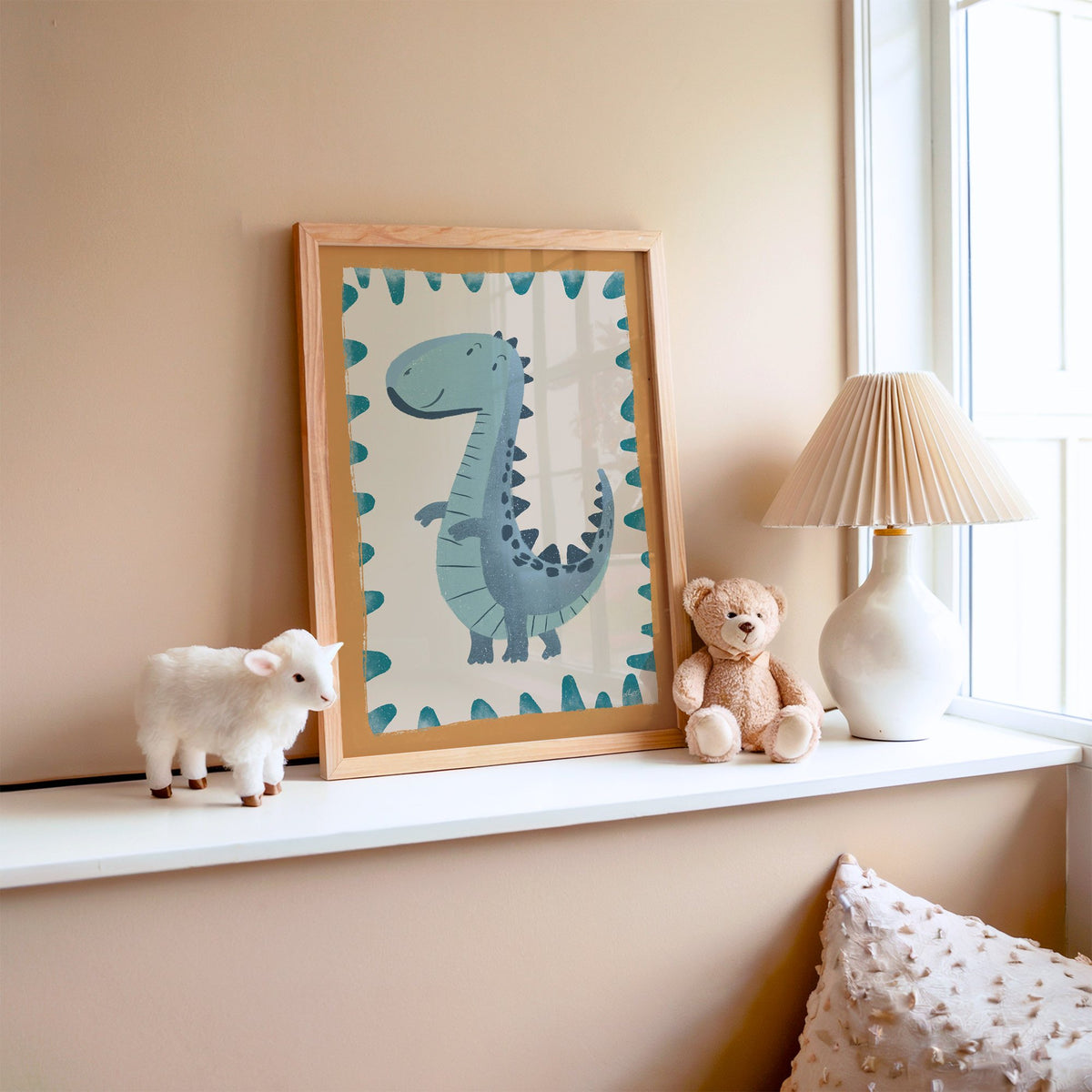Smiling teal dinosaur nursery print in an oak frame on a window ledge with a toy lamb and teddy