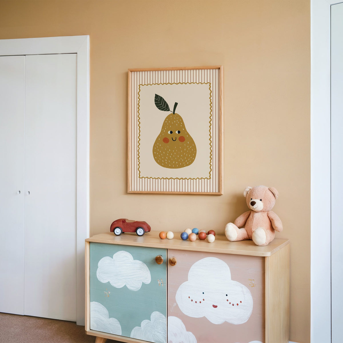 Smiling pear pink stripe nursery print in an oak frame on a peach wall above a cloud-painted cabinet