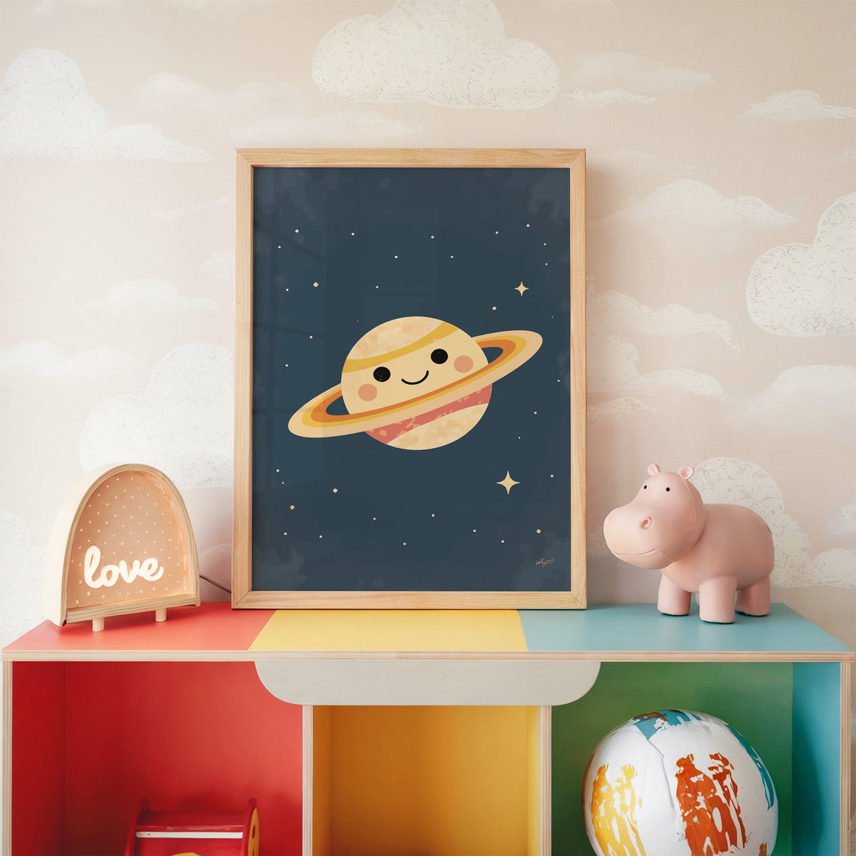 Smiling saturn with rosy cheeks nursery print in an oak frame on a rainbow toy shelf against cloud wallpaper