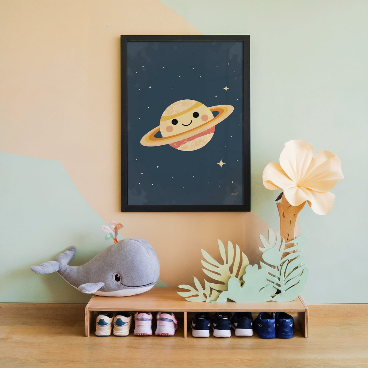 Smiling saturn with rosy cheeks nursery print in a black frame on a mint and peach wall above a whale plush