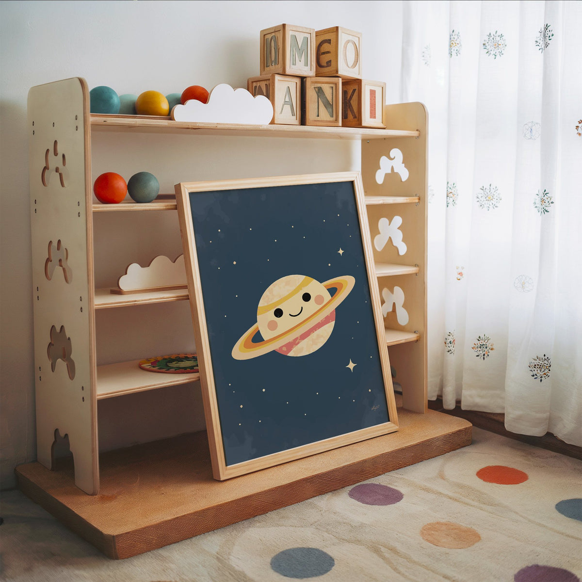 Smiling saturn with rosy cheeks nursery print in an oak frame leaning on a toy shelf with wooden letter blocks