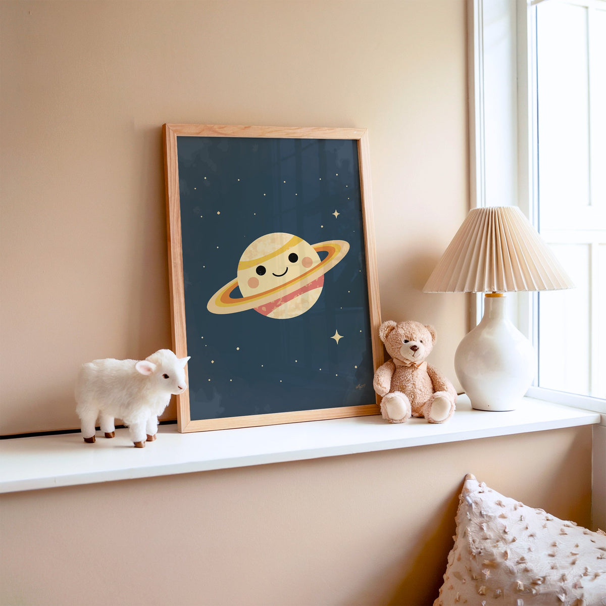 Smiling saturn with rosy cheeks nursery print in an oak frame on a window ledge with a toy lamb and teddy
