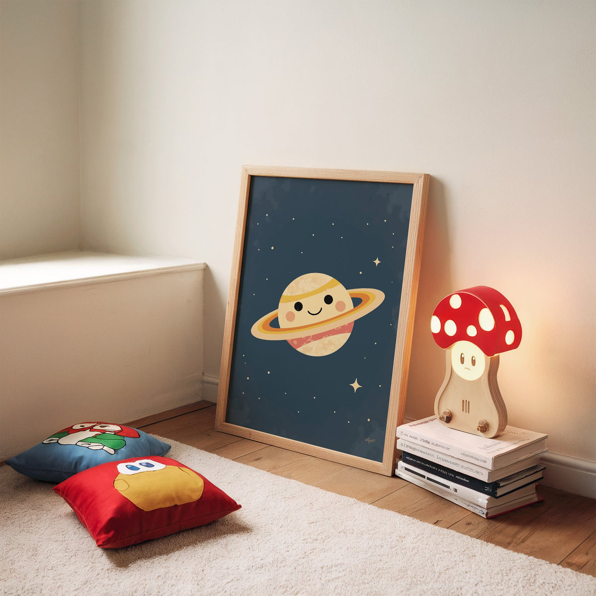 Smiling saturn with rosy cheeks nursery print in an oak frame leaning on a rug beside a mushroom lamp and floor cushions