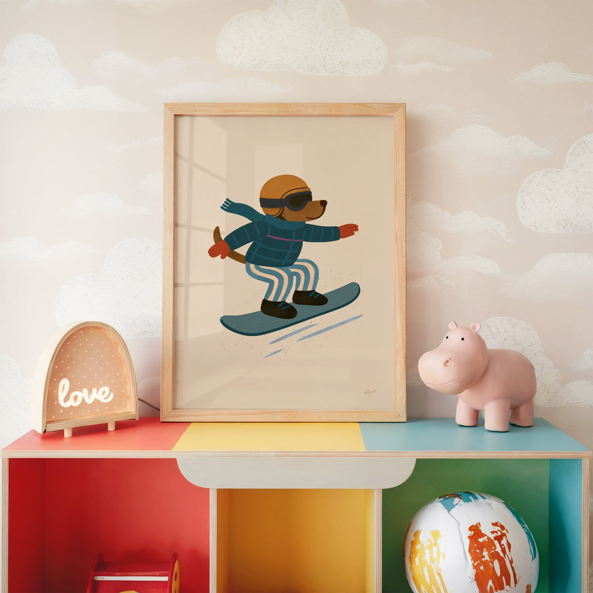 Snowboarding dog with arms wide nursery print in an oak frame on a rainbow toy shelf against cloud wallpaper