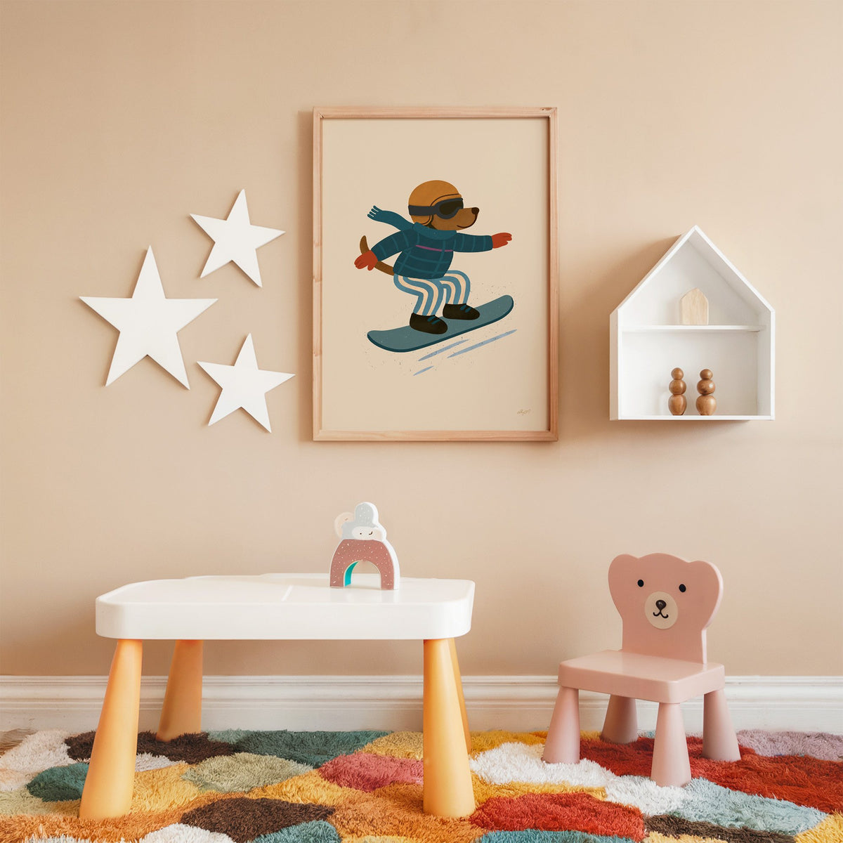 Snowboarding dog with arms wide nursery print in an oak frame on a peach wall above a kids table with wall stars