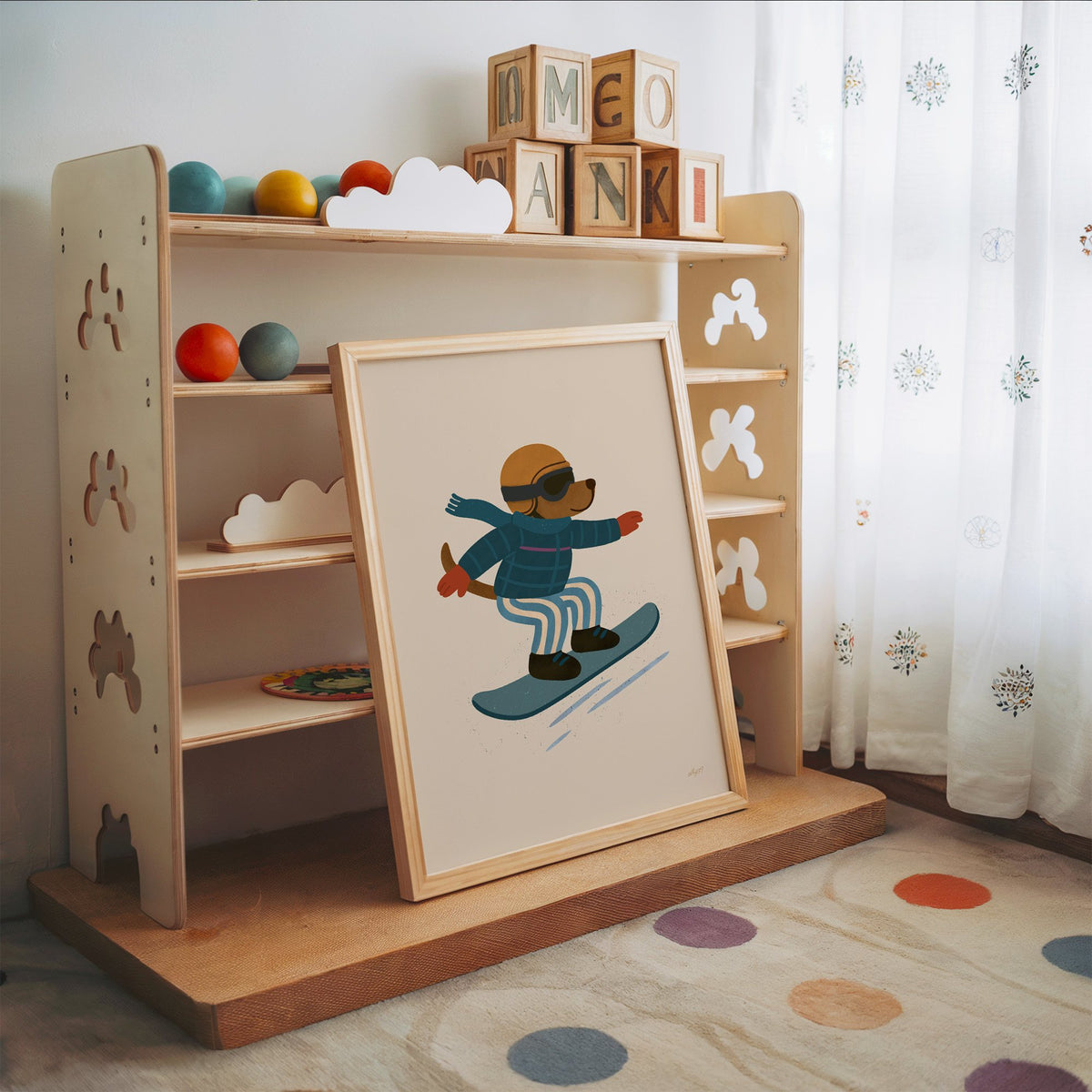 Snowboarding dog with arms wide nursery print in an oak frame leaning on a toy shelf with wooden letter blocks