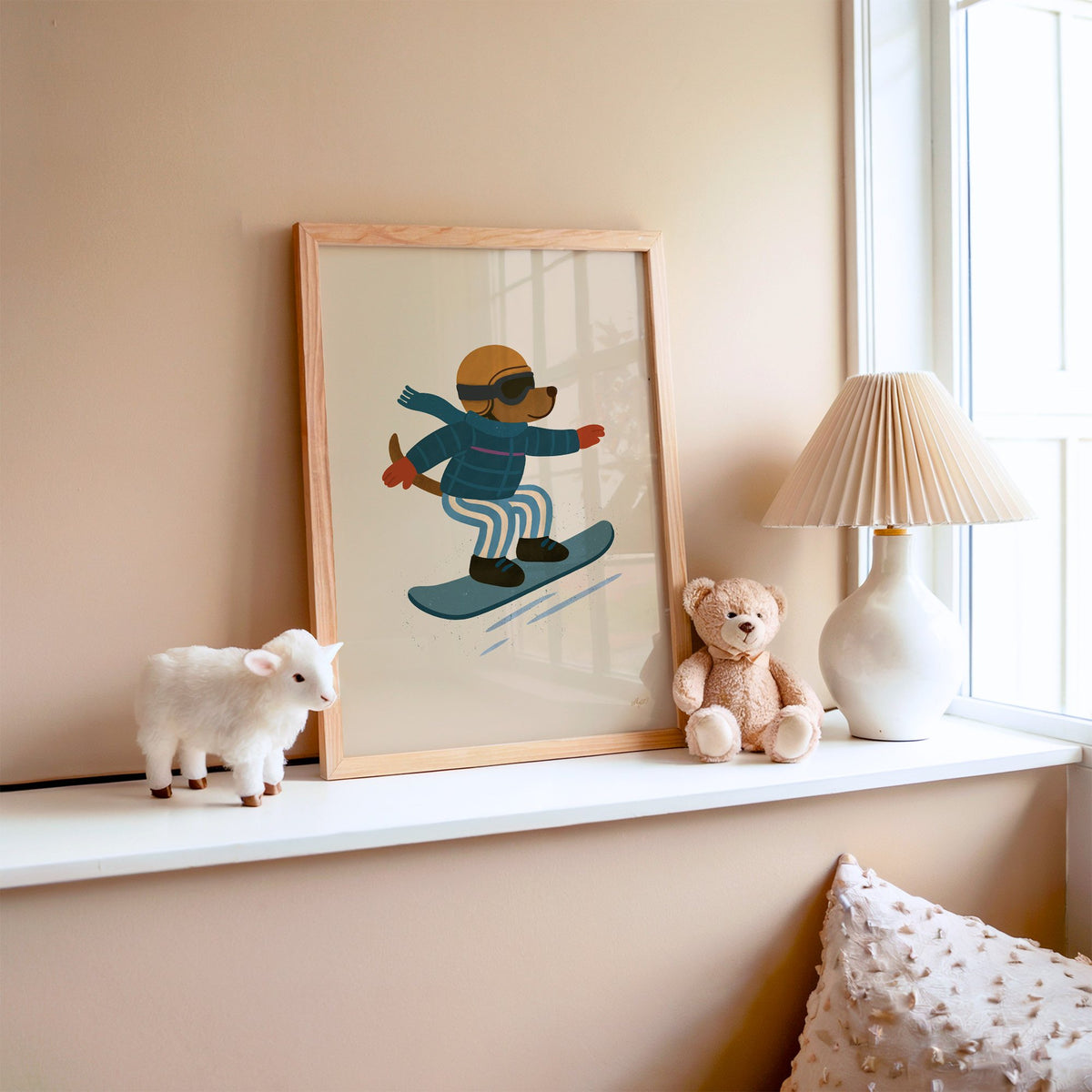 Snowboarding dog with arms wide nursery print in an oak frame on a window ledge with a toy lamb and teddy