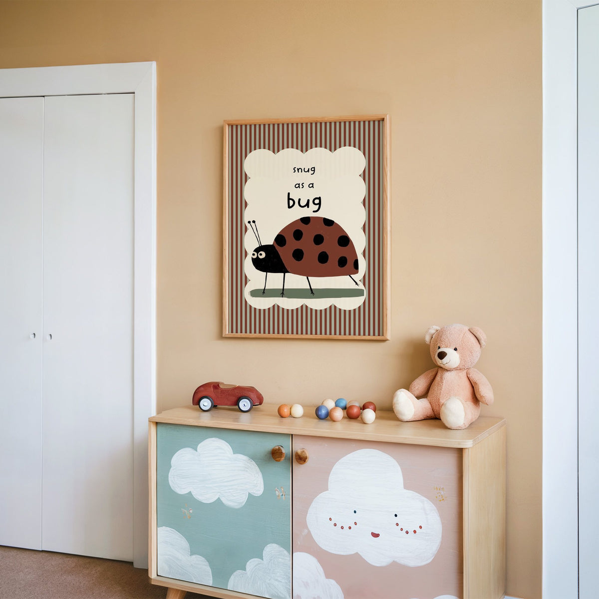 Snug as a bug ladybug nursery print in an oak frame on a peach wall above a cloud-painted cabinet