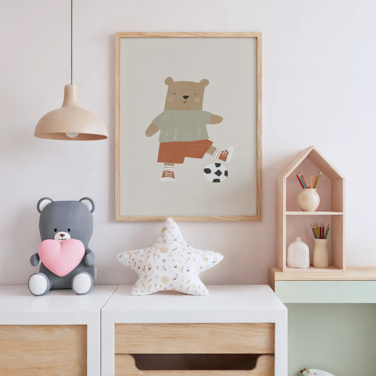 Soccer bear orange shorts nursery print in an oak frame above a white dresser with a star pillow and house shelf