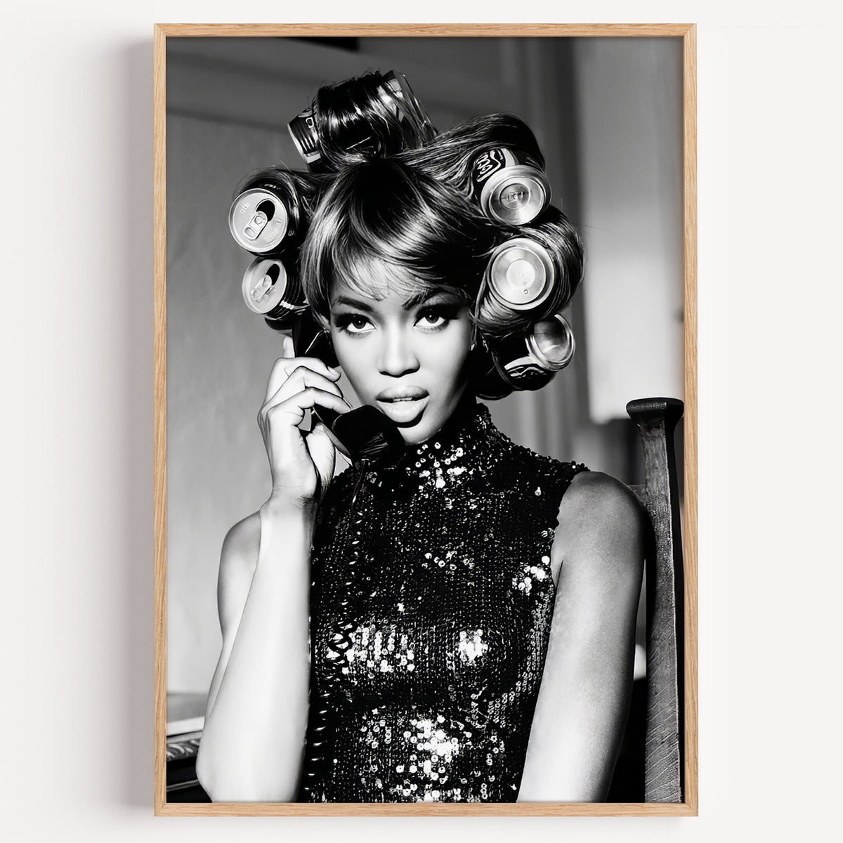 Woman with soda can hair rollers on telephone print in a light oak frame on a plain white wall