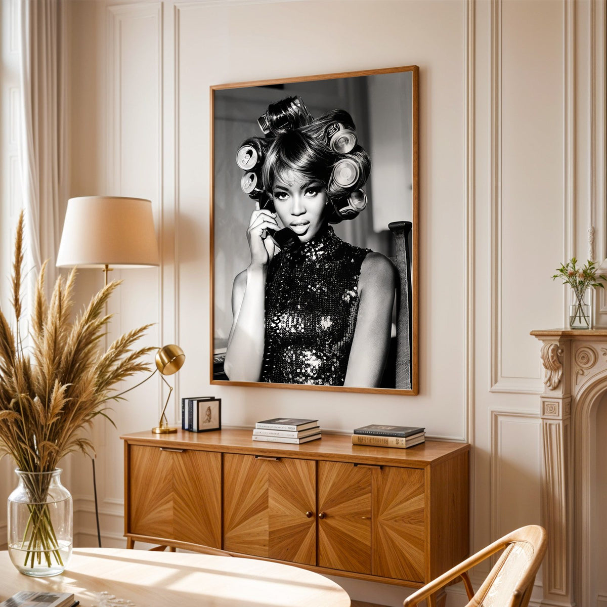Woman with soda can hair rollers on telephone print in an oak frame above a sunburst wood sideboard with pampas grass