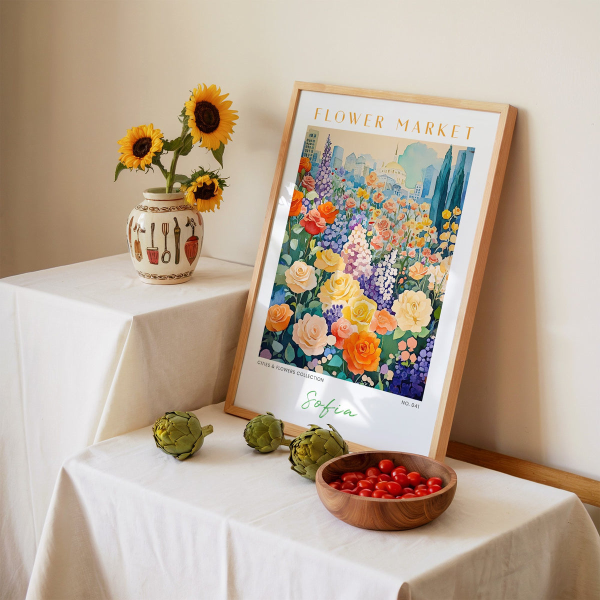 Sofia flower market print in an oak frame leaning on a linen-draped table beside a vase of sunflowers