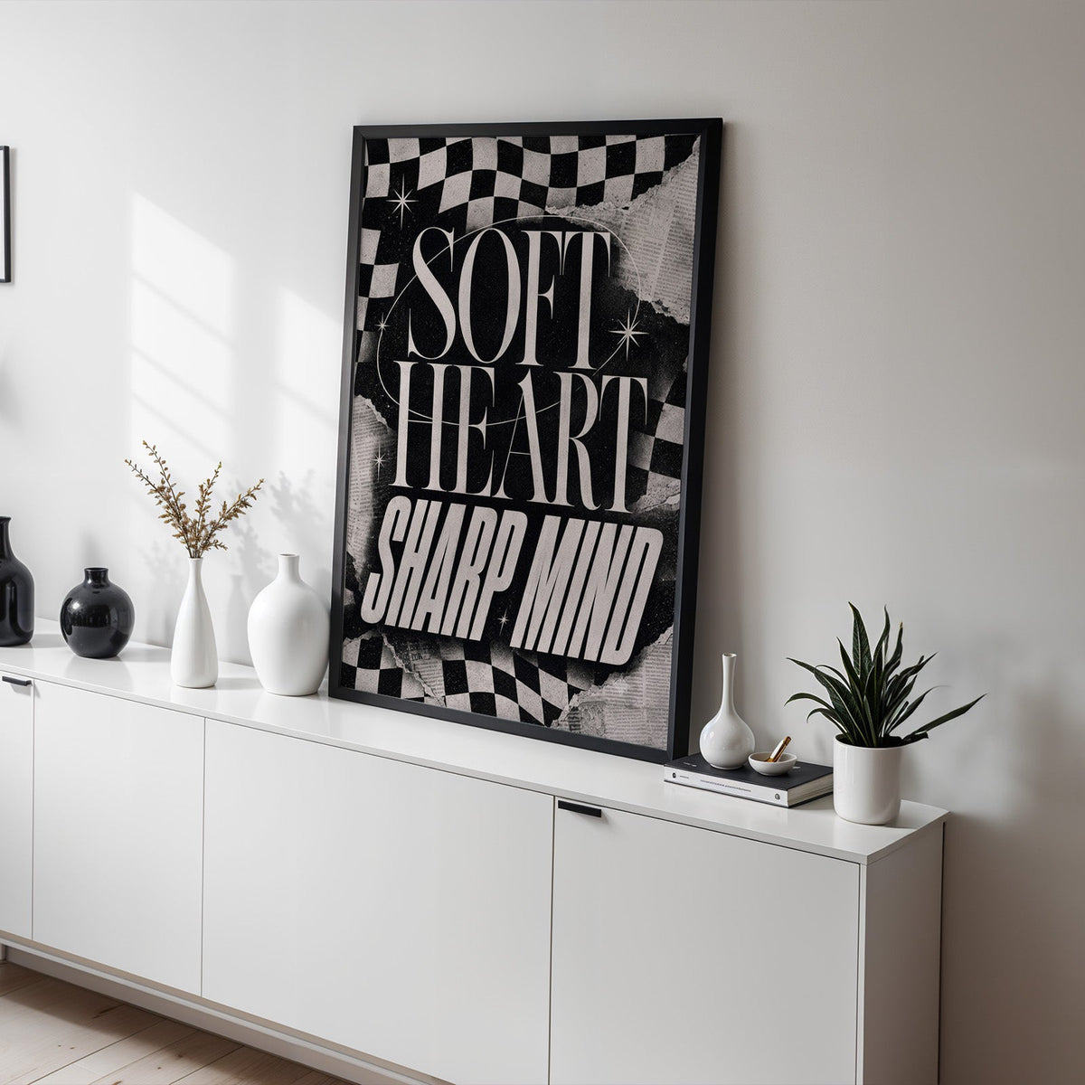 Soft heart sharp mind checkered collage print in a black frame on a white sideboard with black and white vases