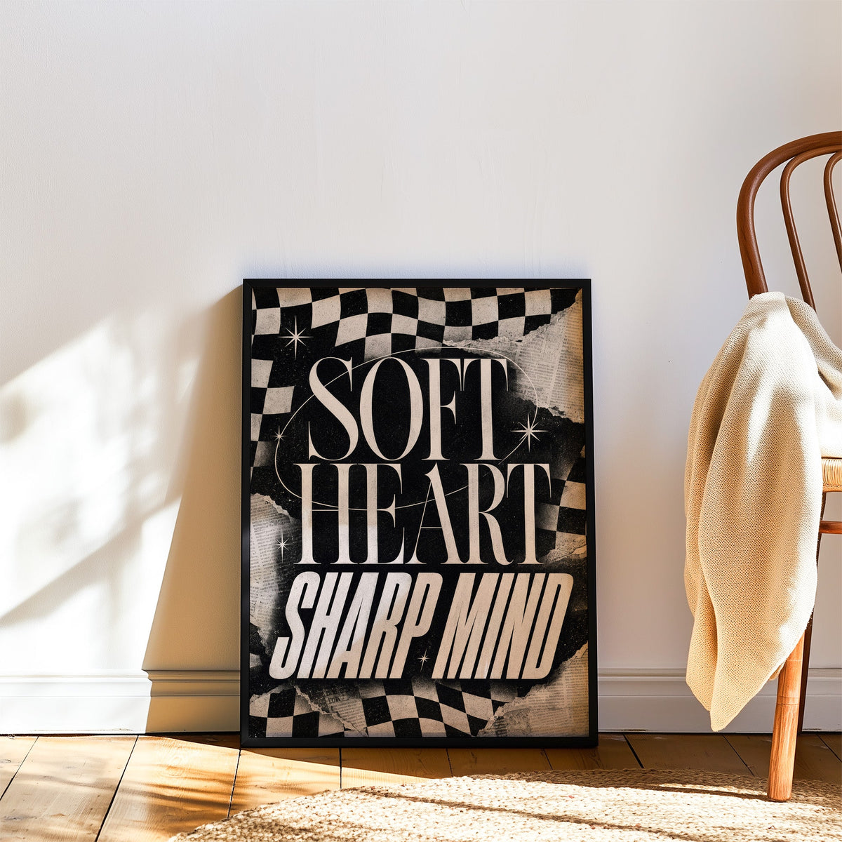 Soft heart sharp mind checkered collage print in a black frame leaning on a wood floor beside a bentwood chair