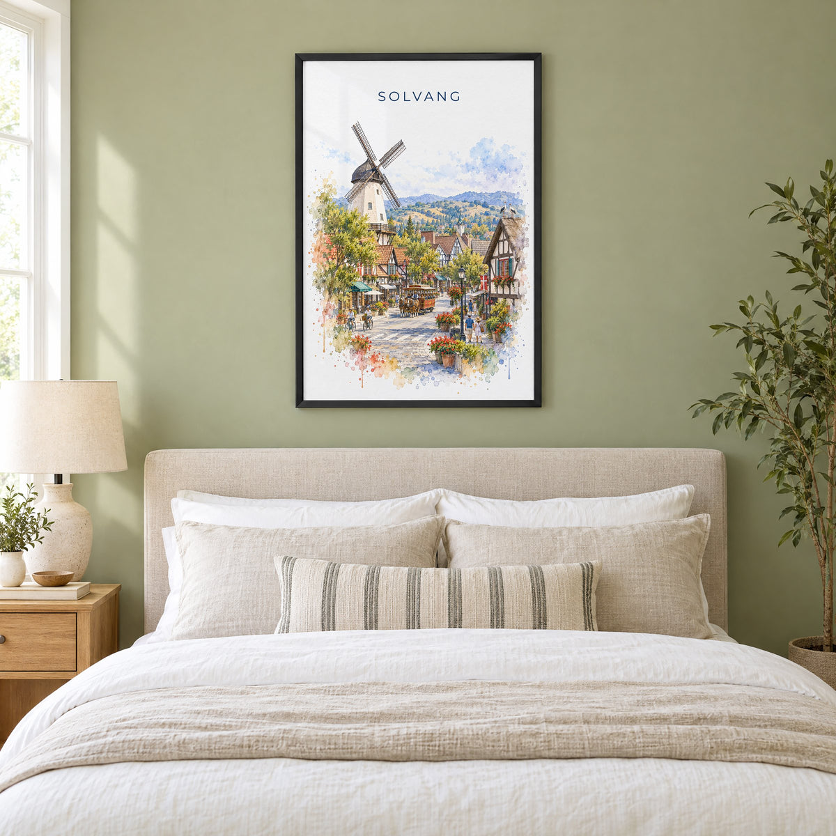 Solvang watercolor print in a black frame above an upholstered headboard in a sage green bedroom