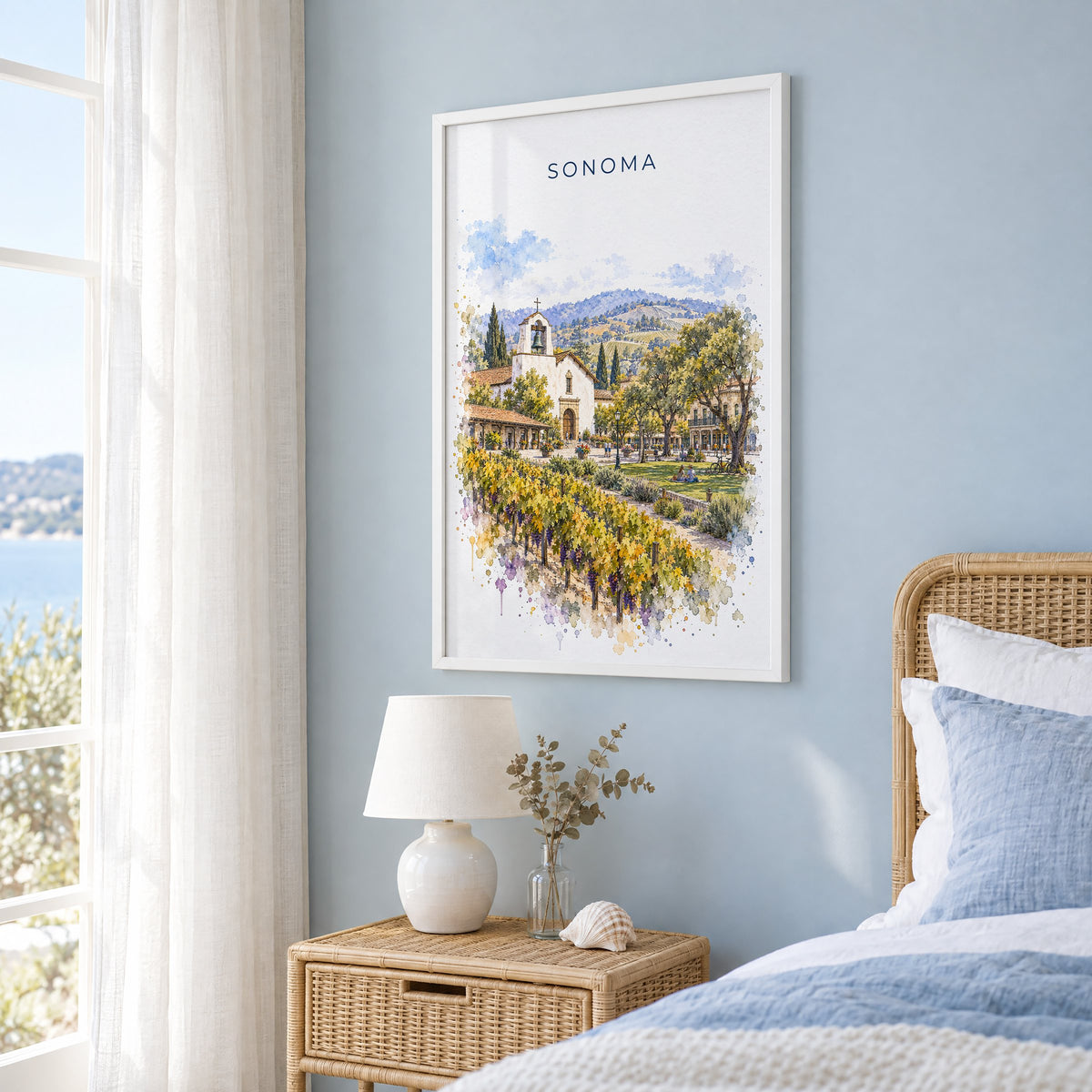 Sonoma watercolor print in a white frame on a pale blue wall beside a rattan bed in a coastal bedroom