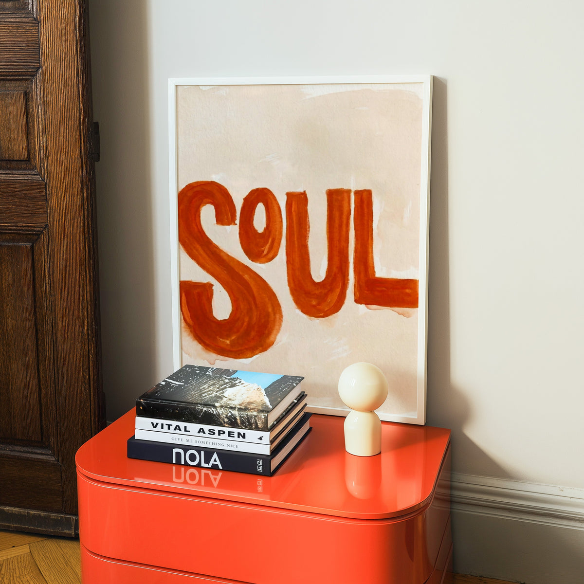 Retro SOUL typography print in a white frame on a glossy orange cabinet with books