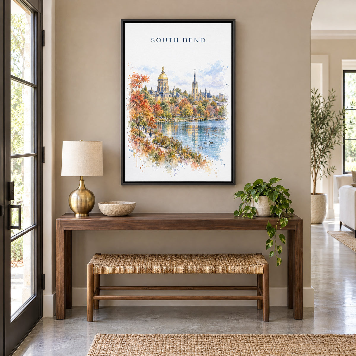 South Bend watercolor print as a black floater canvas above a walnut console and woven bench in an entryway