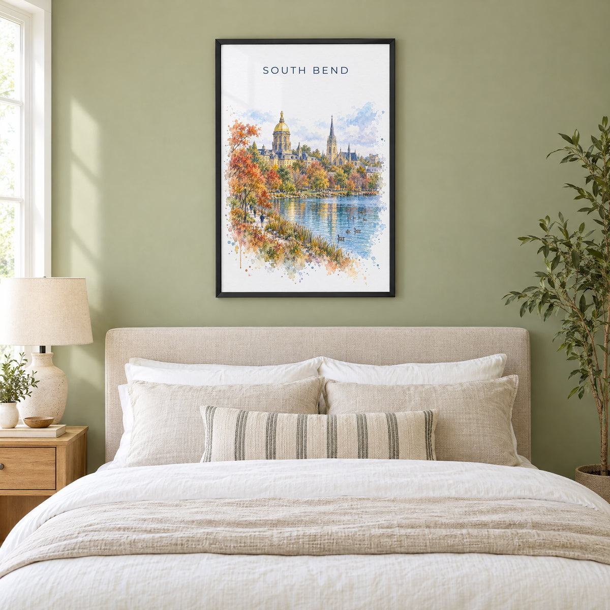 South Bend watercolor print in a black frame above an upholstered headboard in a sage green bedroom