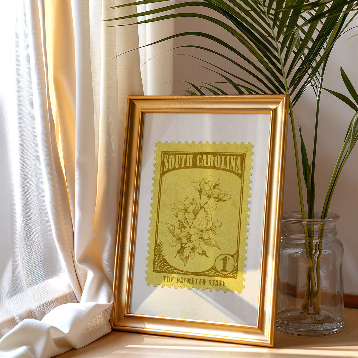 South Carolina stamp print in a gold frame leaning by a cream curtain with a palm in a glass jar