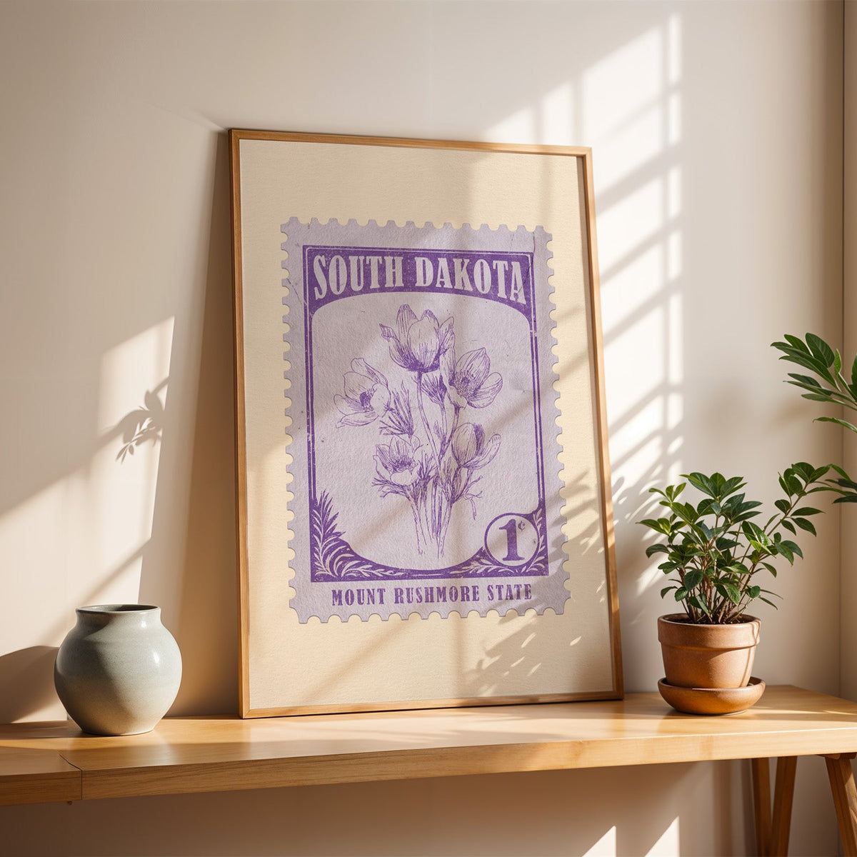 South Dakota Pasque Flower stamp print in a light oak frame leaning on a table beside a stoneware vase