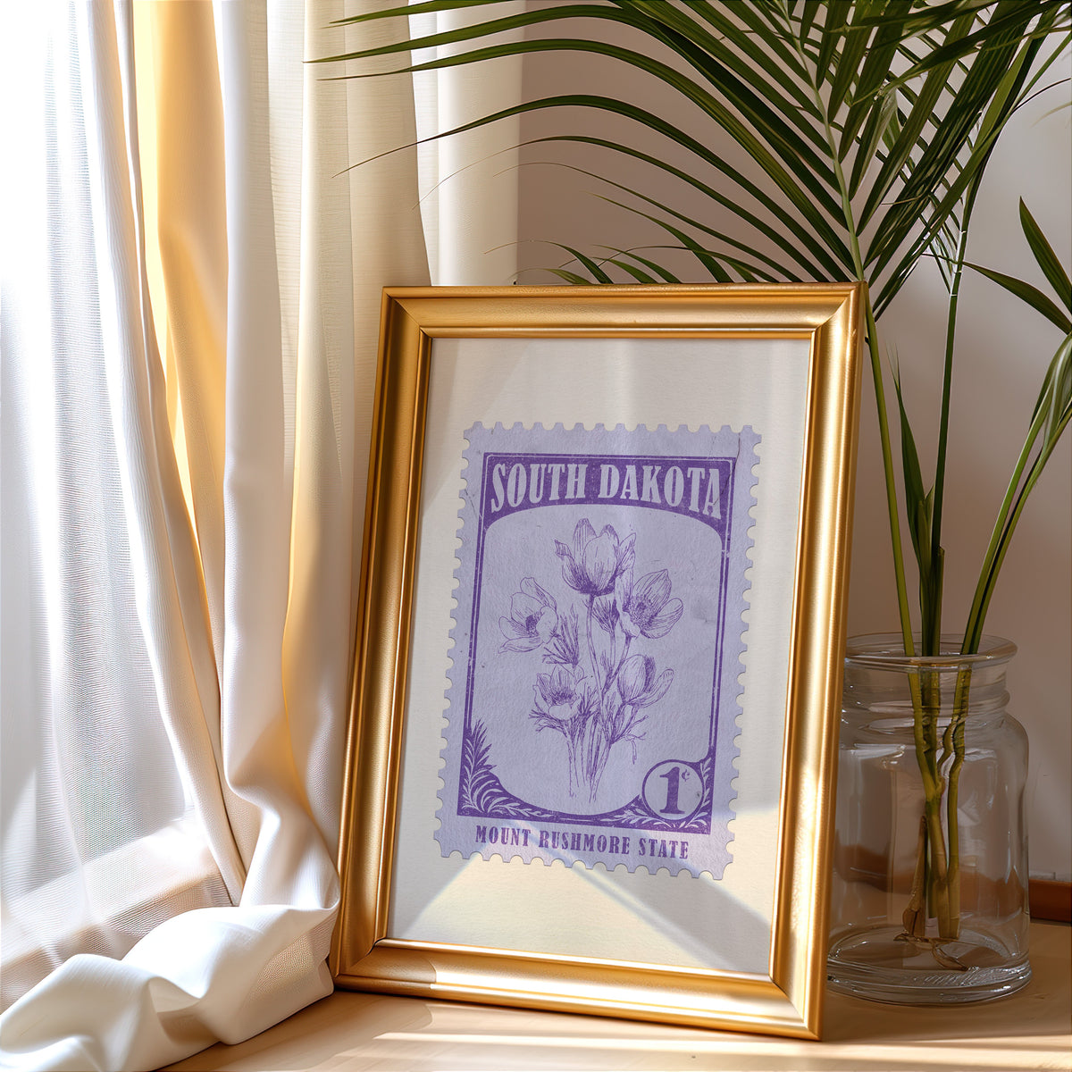 South Dakota stamp print in a gold frame leaning by a cream curtain with a palm in a glass jar