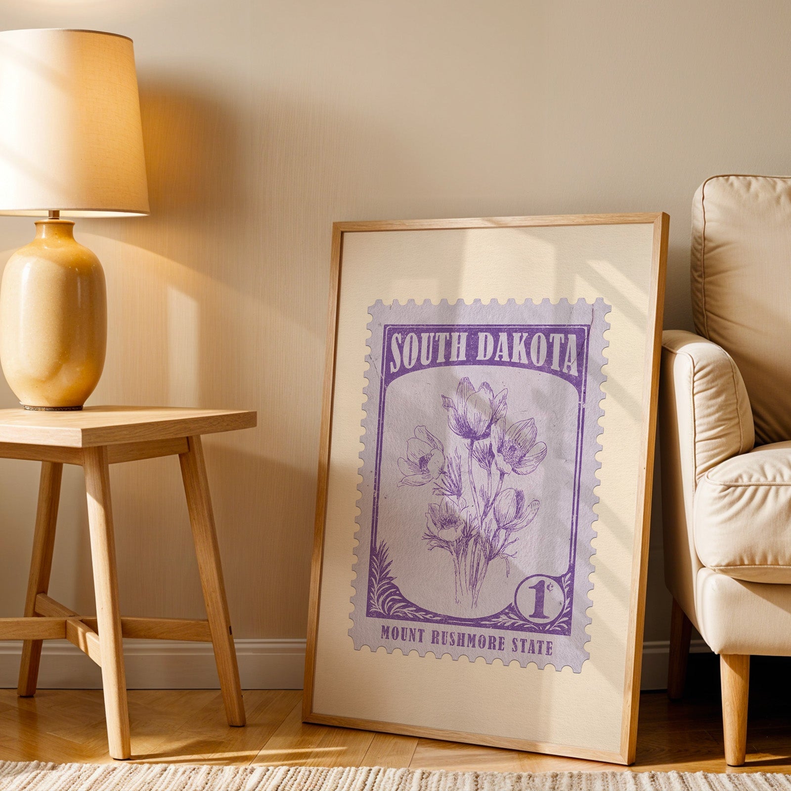 South Dakota stamp print in a wood frame resting on the floor beside a beige armchair and a yellow lamp