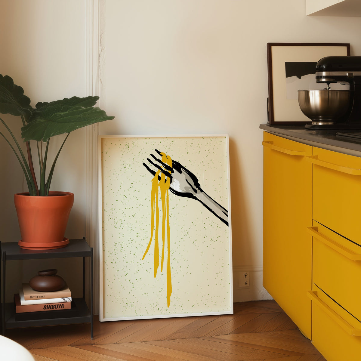 Spaghetti fork print in a white frame leaning on parquet beside a bright yellow kitchen
