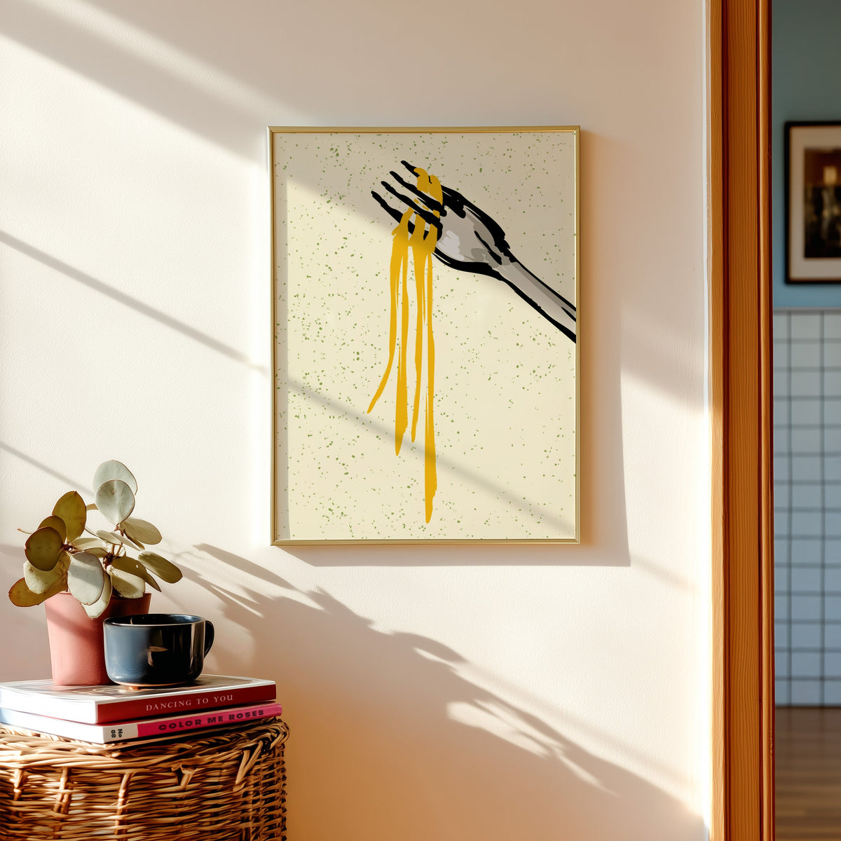 Spaghetti fork print shown in a gold frame above a basket of books and a pilea plant
