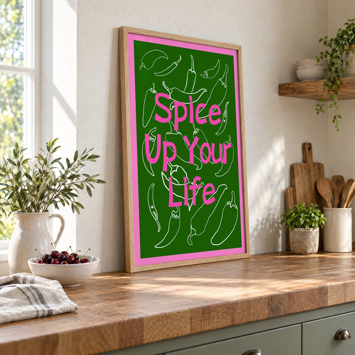 Spice Up Your Life green chilli print in an oak frame leaning on a butcher block island beside a bowl of cherries