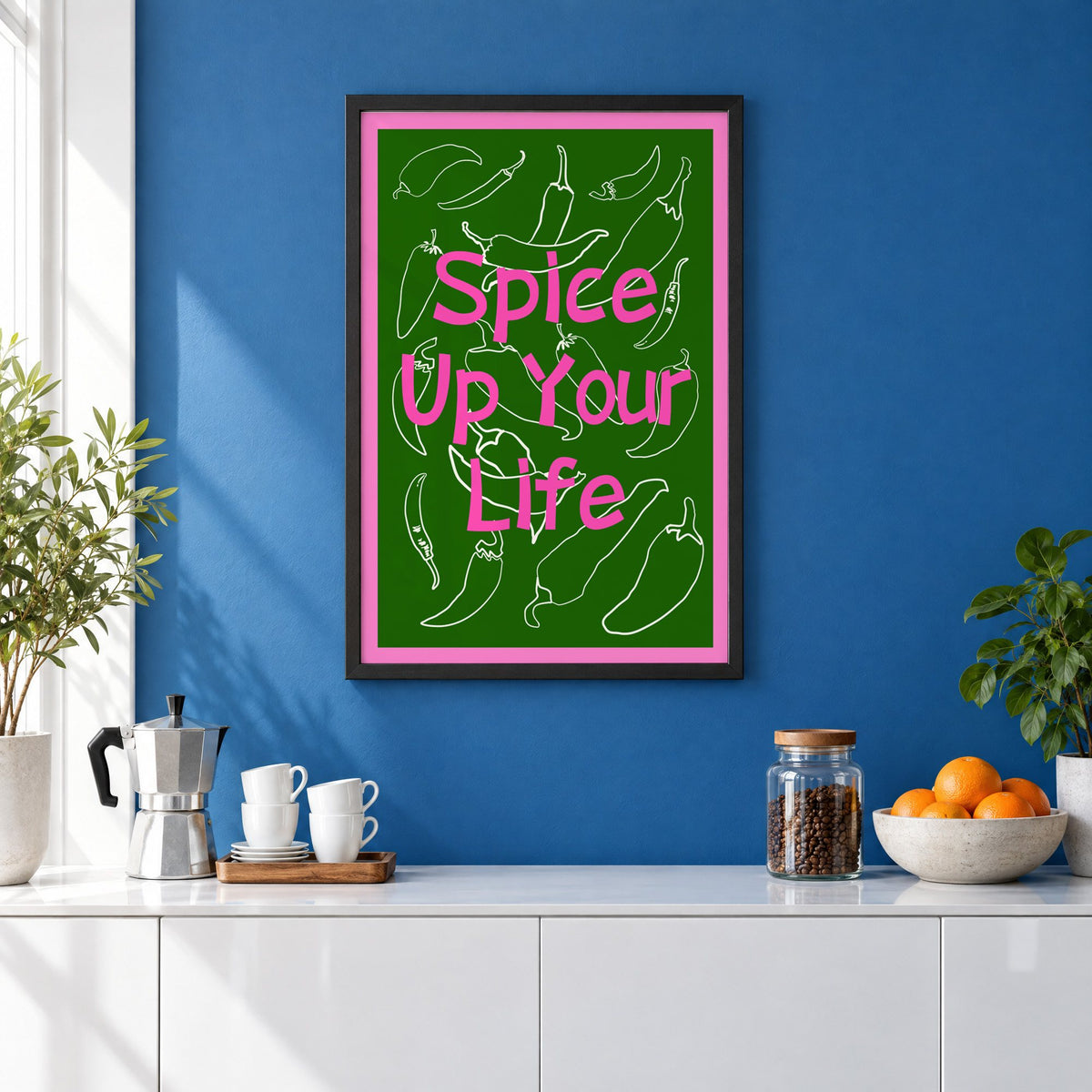 Spice Up Your Life green chilli print in a black frame on a cobalt blue wall above a coffee station