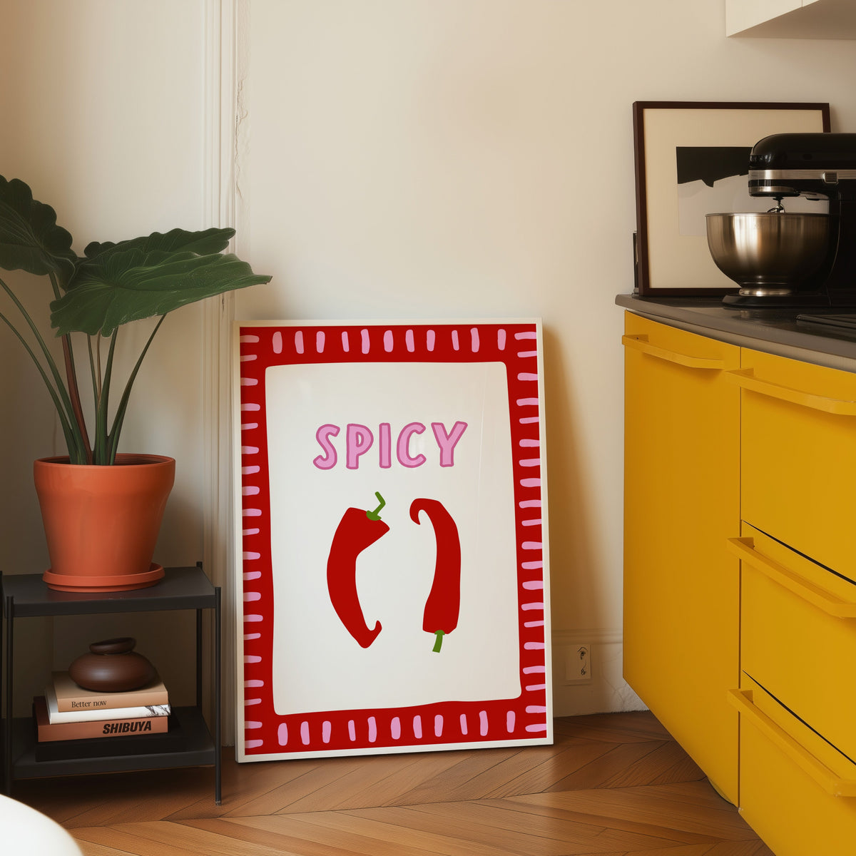 Spicy chilli print in a white frame leaning on parquet beside a bright yellow kitchen
