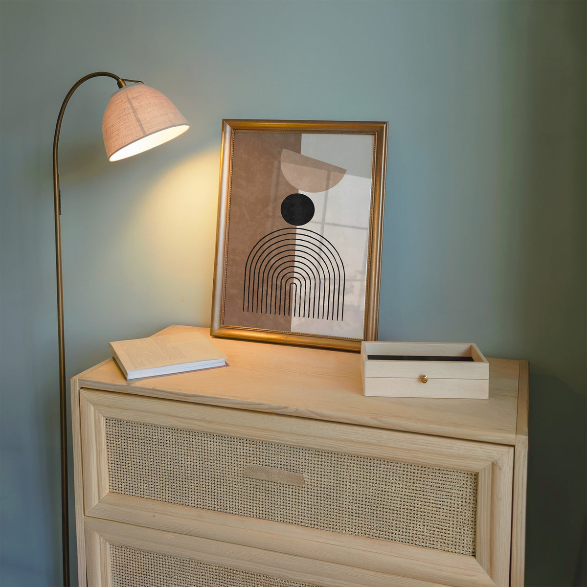 Split brown and cream line arch print shown in a gold frame on a cane dresser lit by a floor lamp