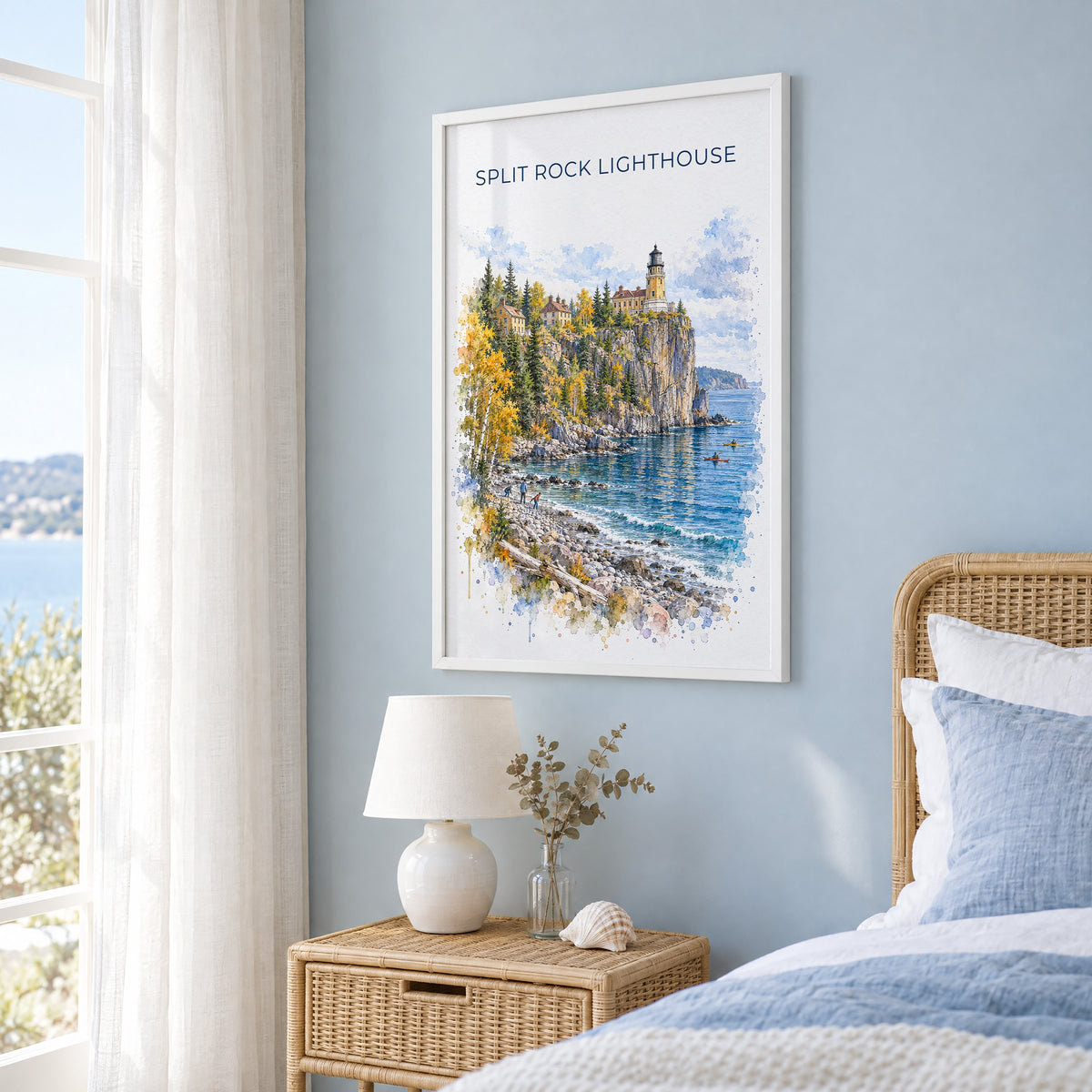 Split Rock Lighthouse watercolor print in a white frame on a pale blue wall beside a rattan bed in a coastal bedroom
