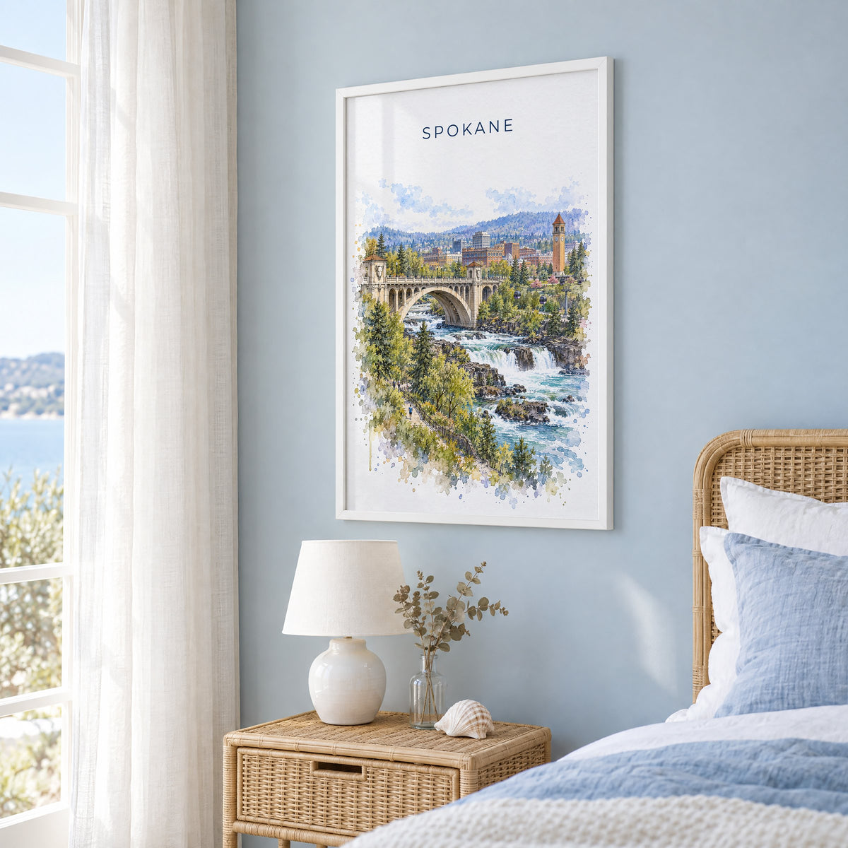 Spokane watercolor print in a white frame on a pale blue wall beside a rattan bed in a coastal bedroom