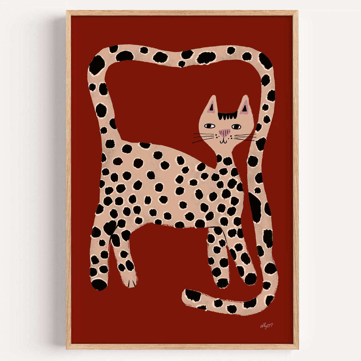Spotted cat with looping tail nursery print in a light oak frame on a plain white wall