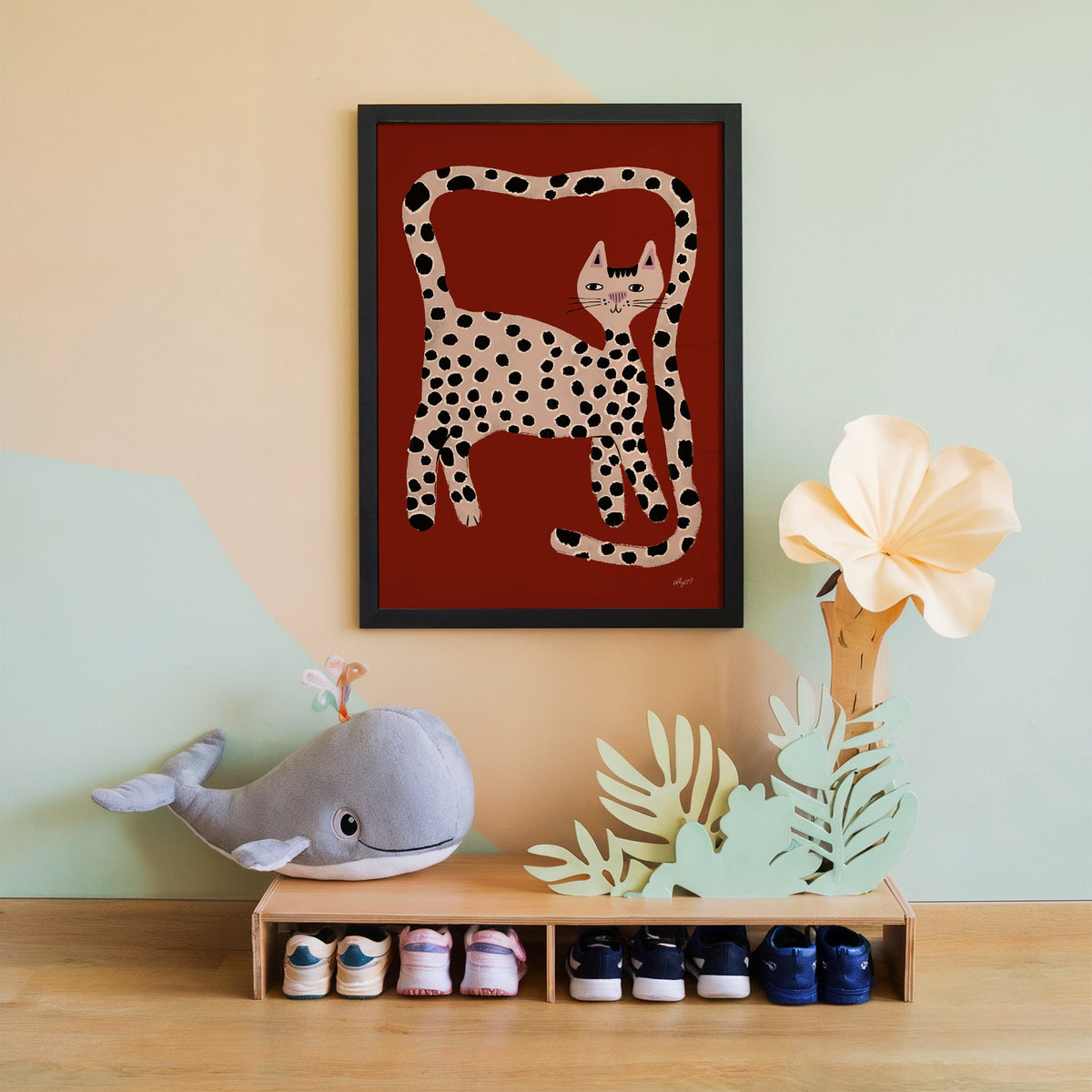 Spotted cat with looping tail nursery print in a black frame on a mint and peach wall above a whale plush
